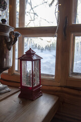 A Christmas lantern and an ancient samovar on a wooden table against the background of a window.