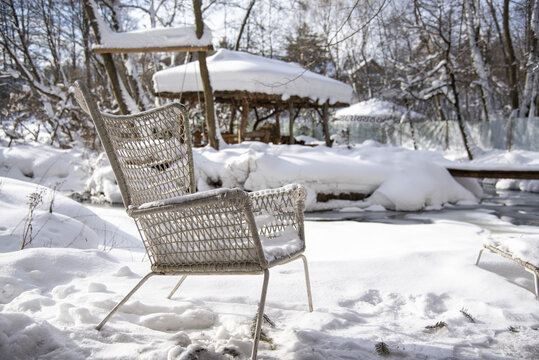 A wicker chair made of painted white rattan in the snow on a clear winter day. Outdoor recreation, garden furniture.