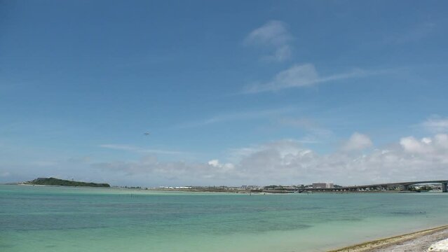 TOMIGUSUKU, OKINAWA, JAPAN - AUGUST 2021 : View of Senaga island beach (Ocean or sea) and airplane in daytime. Clear blue summer sky and clouds. Holiday, vacation and resort concept video.