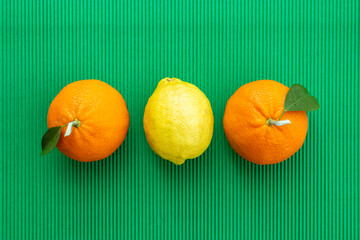 Two oranges with leaves and one yellow lemon on green background