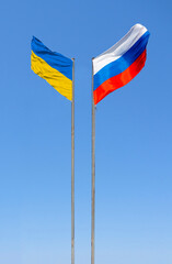 Flags of Russia and Ukraine are flying in the wind against the blue sky