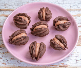 Seven chocolate cookies with brown cream on pink round plate. Image from above