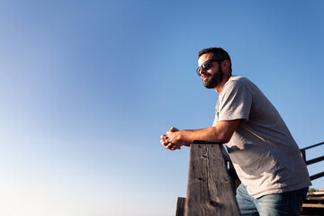 man with sunglasses leaning on a wooden railing