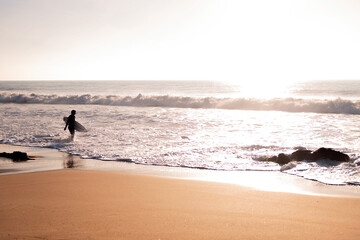 Fototapeta na wymiar silhouette of a surfer walking along the shore