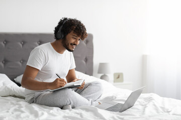 Millennial guy attending webinar from home, using laptop in bed