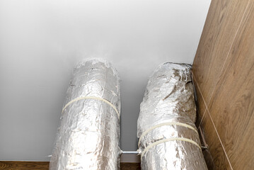 Air intake and exhaust in the home mechanical ventilation with heat recovery with visible insulated pipes with silver foil entering the ceiling.