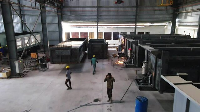 India drone fly inside manufacturing production line factory with workers welding heavy metal for trailer truck production, safety and security asian working class right
