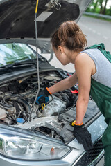 female mechanic wear green uniform checking level of oil on a car engine dipstick