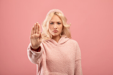 Young serious woman making the hand stop sign against pink background. Stop abuse, discrimination,...