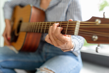leisure, music and people concept - close up of woman playing guitar sitting on windowsill