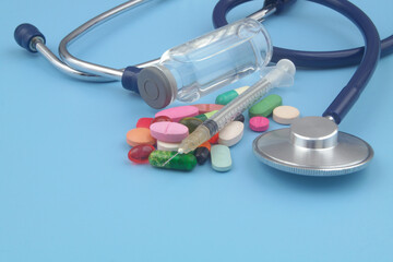 Stethoscope, syringe, vaccine and drugs with pills on blue, space for text. Healthcare and medicine concept.	