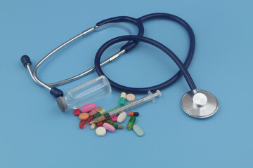 Stethoscope, syringe, vaccine and drugs with pills on blue background. 