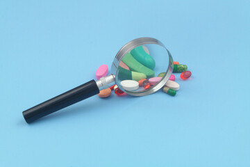 Drugs with magnifying glass on blue background. Review drugs concept.	