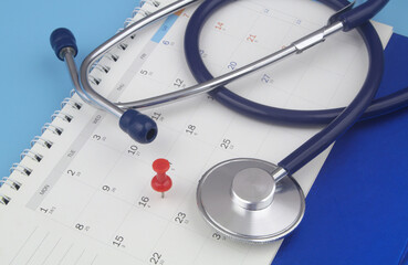 Stethoscope and red push pin on calendar on blue background	