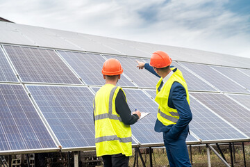  businessman in uniform and helmet tells the worker the plan on which to install solar panels.