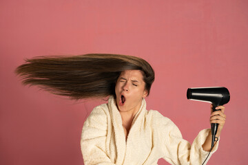 Funny woman drying her long hair with electric fan