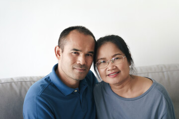 Fototapeta premium Portrait of Asian mature couple sitting in the living room. wife and husband hugging, holding hand with happiness and cheerful. Love, safety, and insurance family concept.