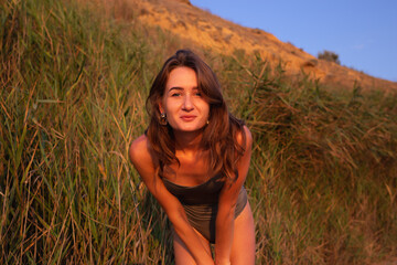 young beautiful woman in a halter swimsuit walks along the beach at sunset