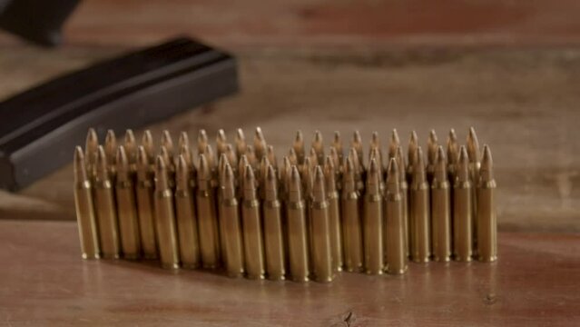 High angle dolly out of 5.56mm ammunition, slowly revealing an AR-15 in the background