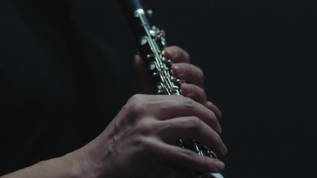 Man in a black shirt blows air into the clarinet while playing the instrument with his fingers by covering and opening several holes. Close up shot