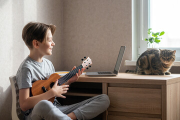 An 11-year-old boy plays the ukulele. Learning to play a musical instrument online.