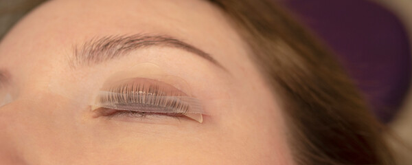 Woman on the procedure for eyelash extensions, lamination in beauty salon. Cosmetologist applying glue on woman's lashes. Close-up of girl face during lash lift laminating botox set. 