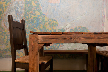 An old wooden table and chair. In the background is a colorful, cracked, dingy wall. Rustic interior.
