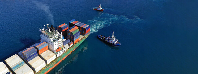 Aerial drone ultra wide photo of tug boats manoeuvring container ship by pushing or pulling near...