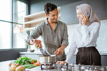 muslim couple cooking their food in the kitchen while wife taking a phone call