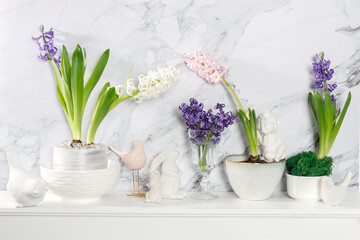 White hyacinth in a large porcelain bowl, figurines of hares and a bird, are on the fireplace against the white marble wall. Layout. Spring concept