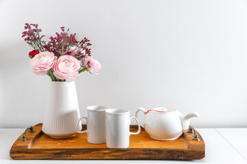 Persian pink buttercup with the wooden brown tray on a white table. Time to drink tea. Ceramic teapot and two porcelain cups. Copy space