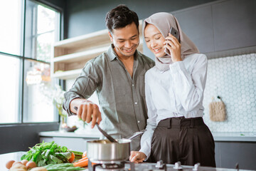 muslim couple cooking their food in the kitchen while wife taking a phone call