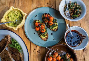 Stock photo wooden table with veggie plates, torradas with avocado, cherry tomato, tofu, spinach, pine nuts and berries.