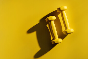 a pair of yellow dumbbells lit by the sun on a yellow background with copy space.