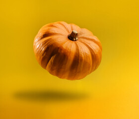 Pumpkin levitating on a yellow background with copy space.