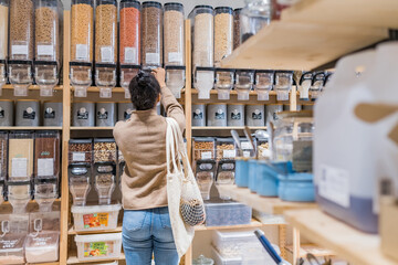 African american woman buying organic cereals and grains in sustainable zero waste grocery store. Young woman refilling reusable container in local grocery store. Rear view