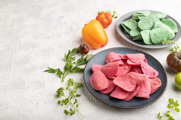 Green and red potato chips on gray concrete background. Side view, copy space.