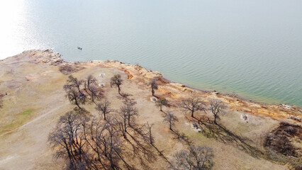 Fototapeta premium Small boat fishing near curved rocky shoreline with drop-offs, cliffs and bluffs at at Grapevine Lake, Texas, America