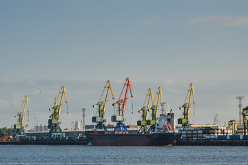 Fototapeta premium Container cargo ship on the water and loading cranes on the sky background at industrial port. Import export business logistic for international trading. Naval transportation of goods concept. photo