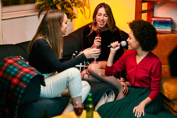 Multicultural group of friends singing on the microphone and having karaoke night at home.