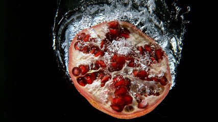 Fresh pomegranate falling into water, freeze motion, underwater view.