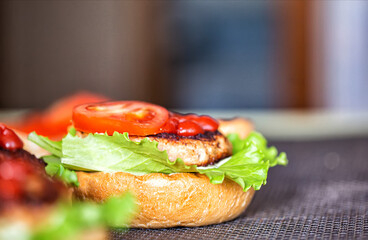 Cooking delicious homemade burgers with cutlet, salad, tomato and sesame burger bun, close-up. Delicious homemade food, fast food. Copy space for text