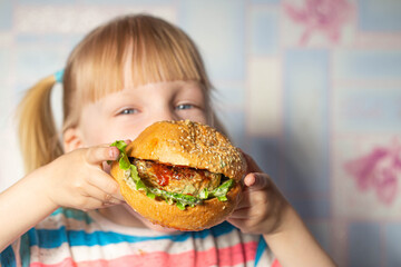 4 year old caucasian girl eating a big hamburger cooked at home. Copy space for text