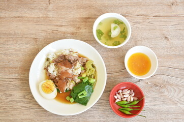 braised slice pork leg stew black Chinese herb soup topping brown boiled egg half cutting eat couple pickled cabbage and kale dipping mixed spicy sour chili sauce on plain rice in white plate