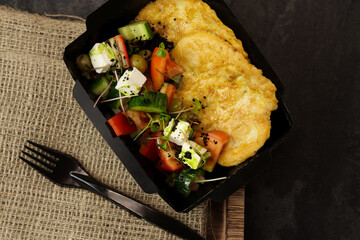 Healthy food delivery concept. Chicken schnitzel with Greek salad in an eco paper container on a black background with burlap. Restaurant dish delivery. Top view. Free space for text.