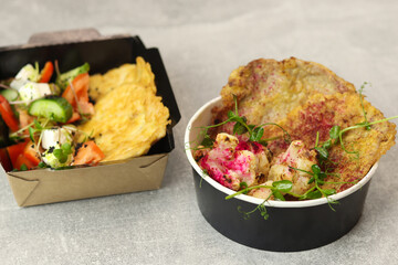 Healthy food delivery concept. Chicken schnitzel with Greek salad in an eco paper containers on a gray background with burlap. Restaurant dish delivery. Top view. Free space for text.