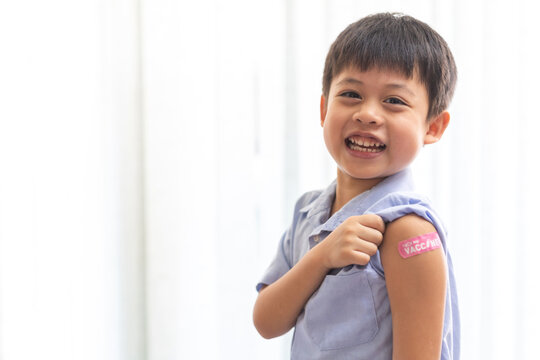 Portrait of happy smile vaccinated little asian kid boy children ages 5 to 11 years old posing show arm with medical plaster after Injection vaccine Covid-19 protection.coronavirus vaccination kid