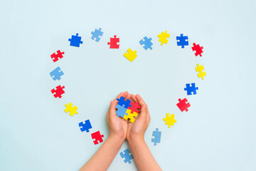 World autism awareness day. Autistic Pride Day. Hands of a small child holding colorful puzzles on blue background. Heart of puzzles.