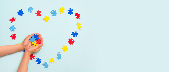 World autism awareness day. Autistic Pride Day. Hands of a small child holding colorful puzzles on blue background. Heart of puzzles.