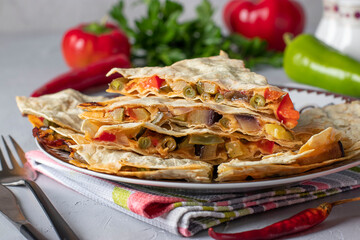 Mexican tortilla quesadilla appetizer with vegetables and cheese in plate on light gray background